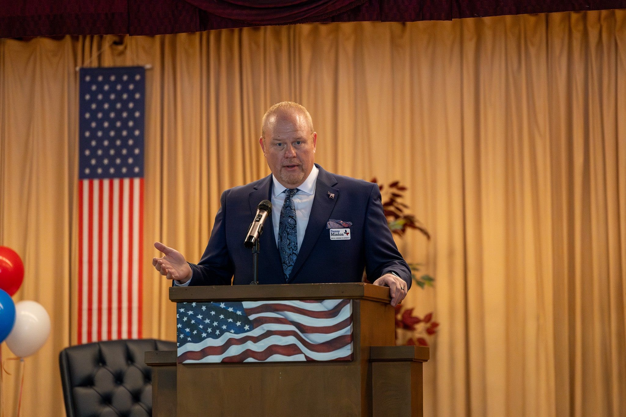 Danny Minton speaking at a podium in front of an American flag